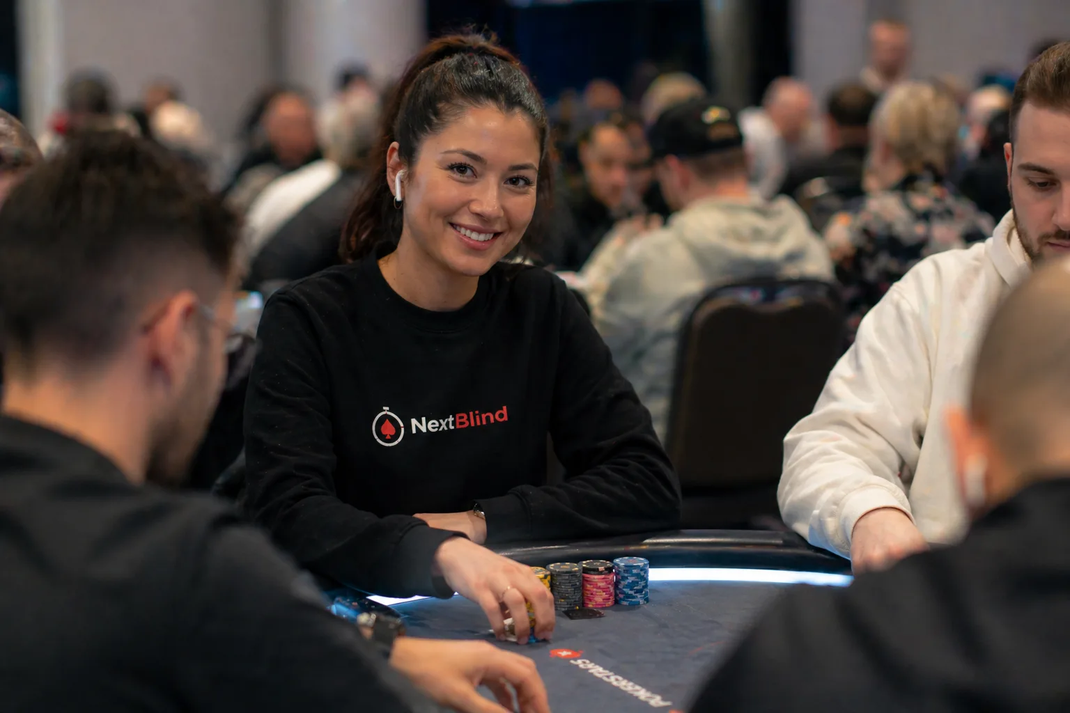A smiling poker player wearing a NextBlind hoodie at a live tournament table